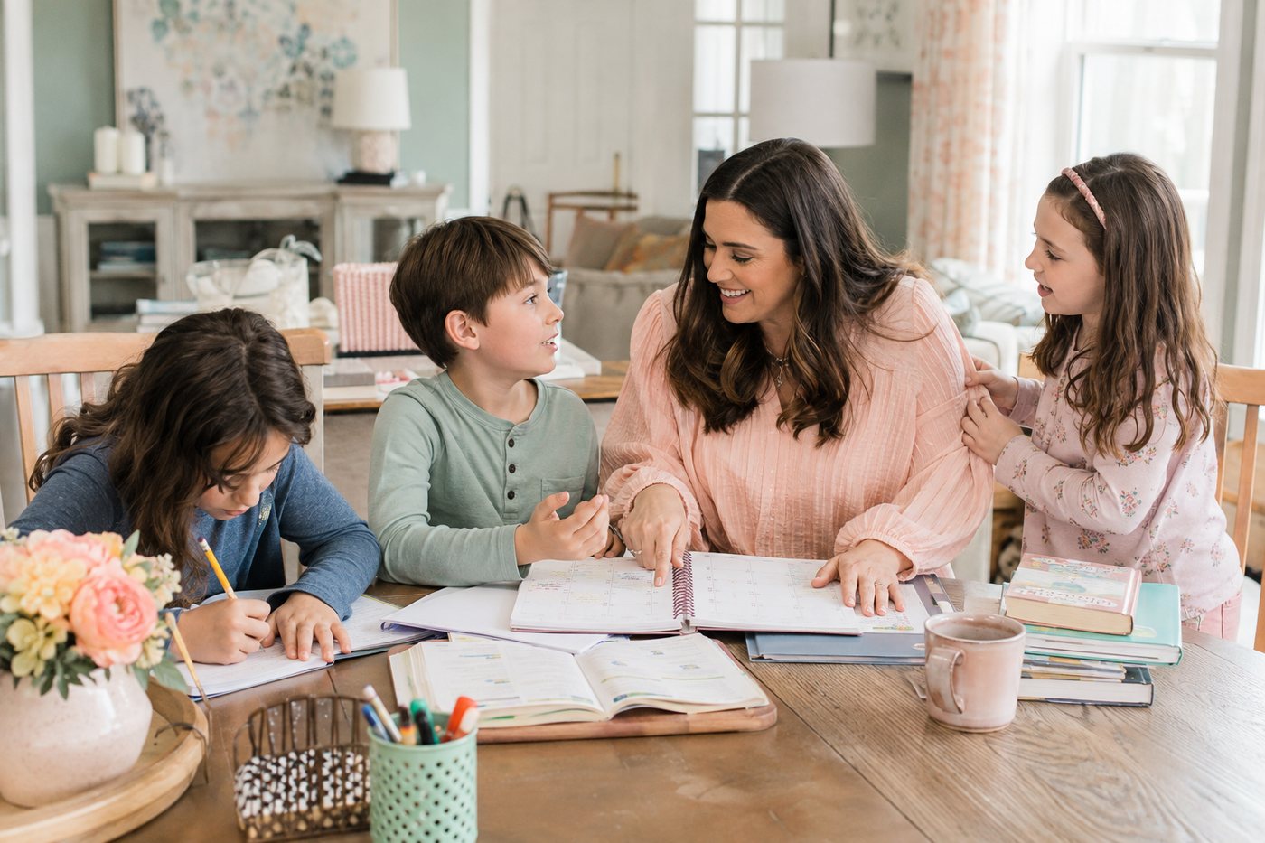 Three children gathered around a parent pointing at the month on a family calendar.