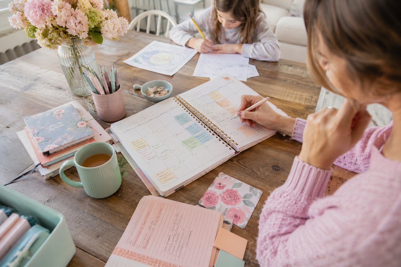 Filling in a monthly spread with sticky notes while a child works across the table.