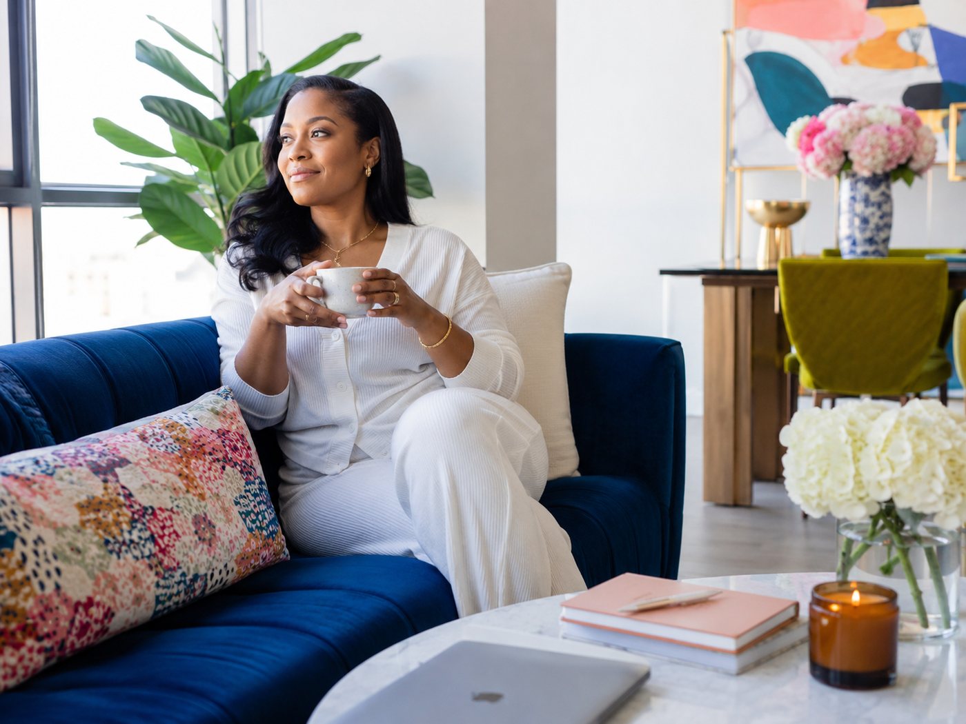 A woman resting with a cup of tea in a bright living room.