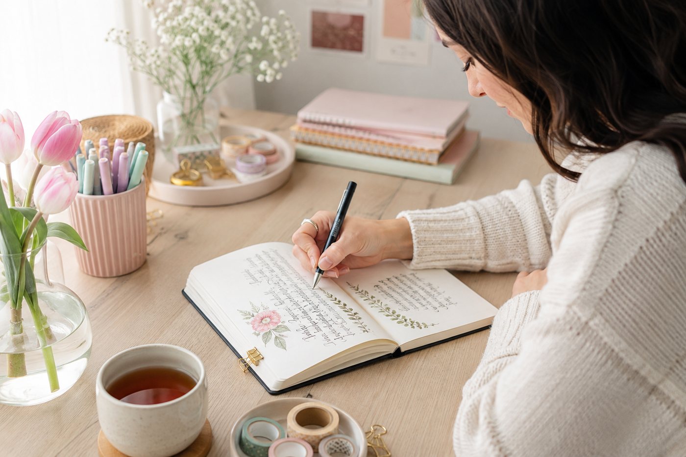 Hand-lettering a journal page at a desk with tulips and coloured pens.